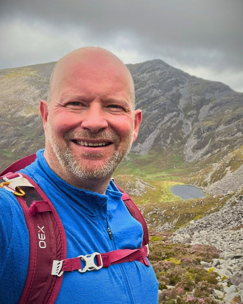 Matt hiking on a mountain trail with scenic countryside views